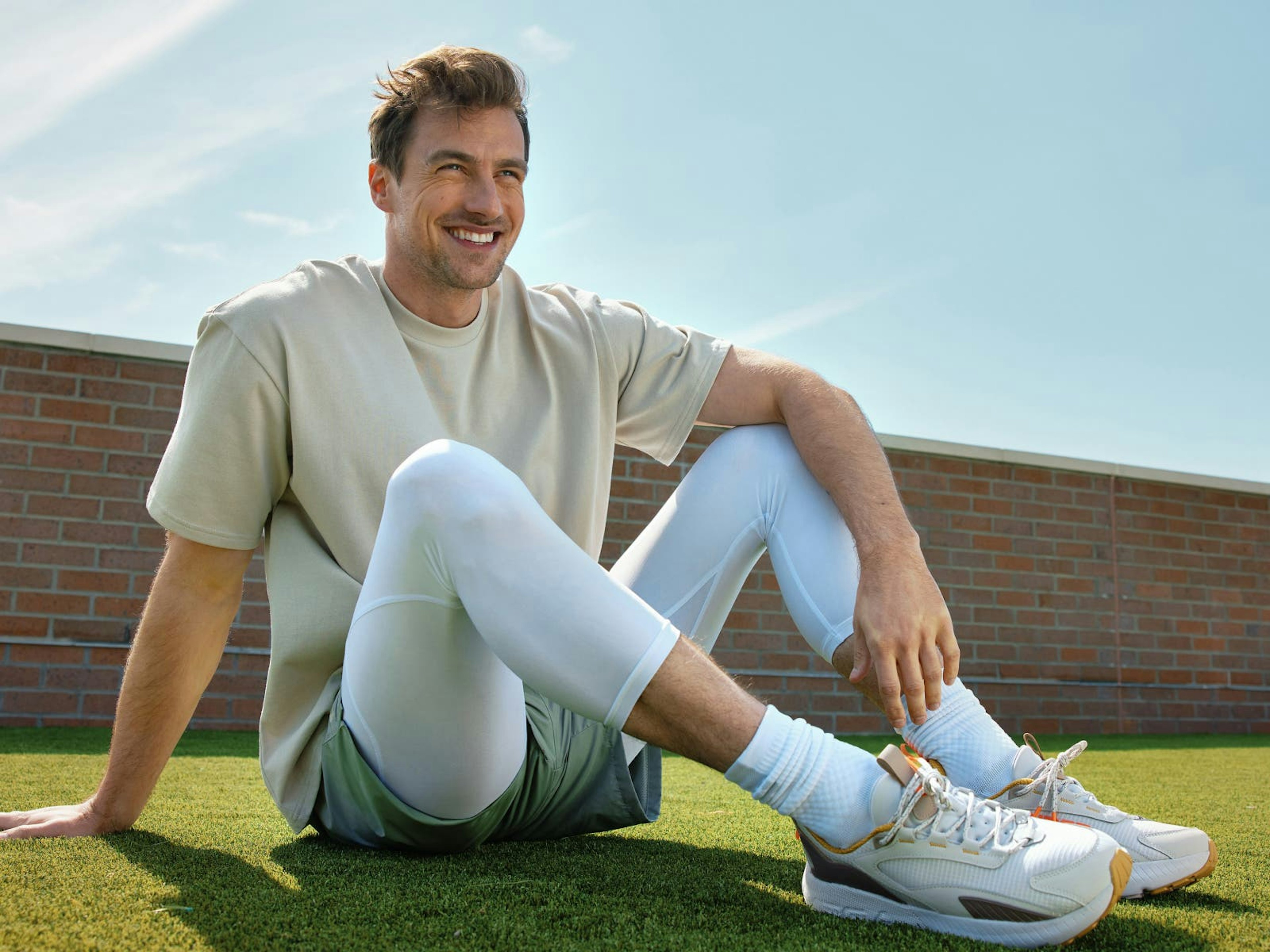 man sitting in tan shirt green shorts and white athletic tights