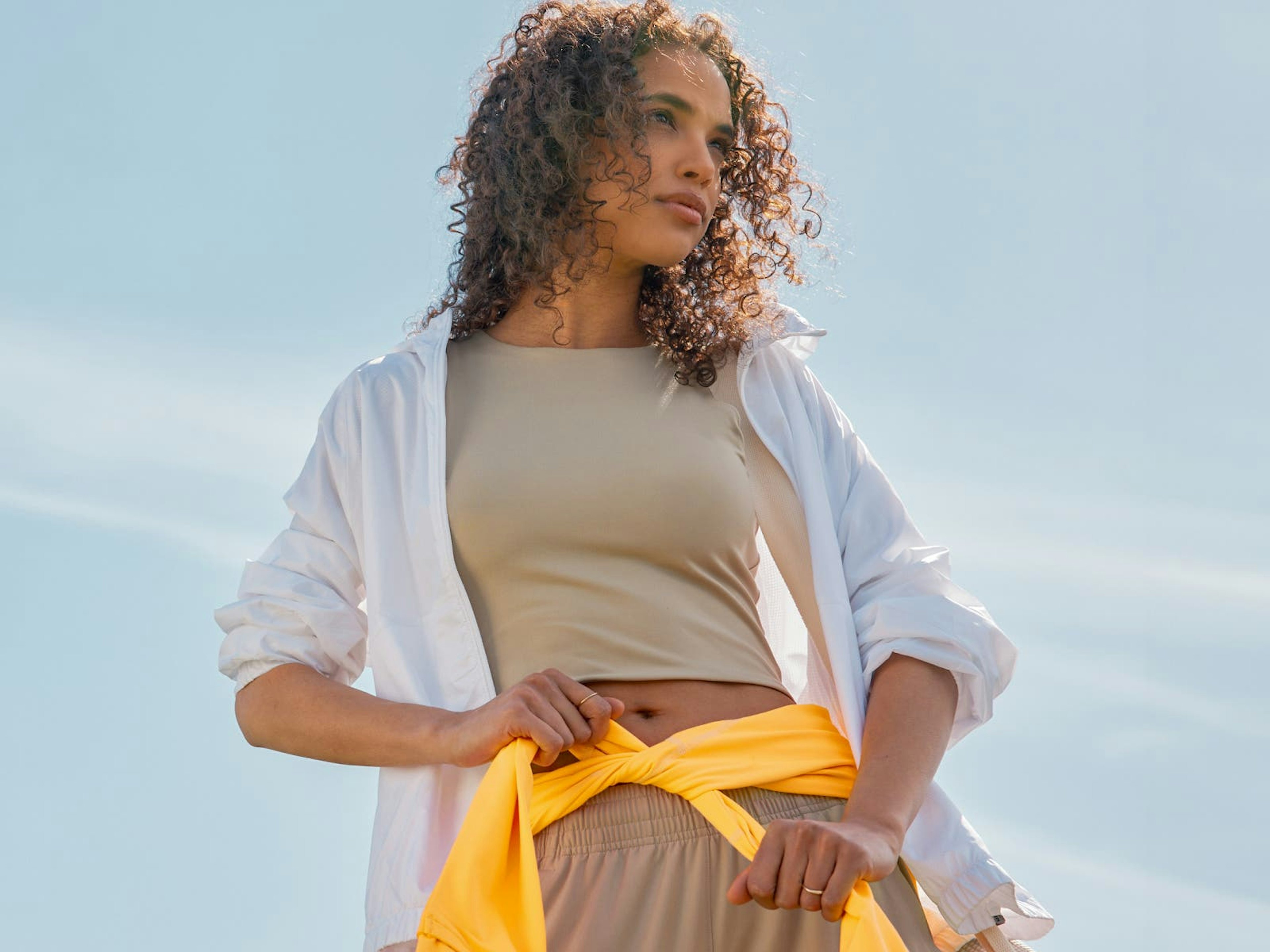 woman in tan athleisure outfit with yellow jacket tied around waist